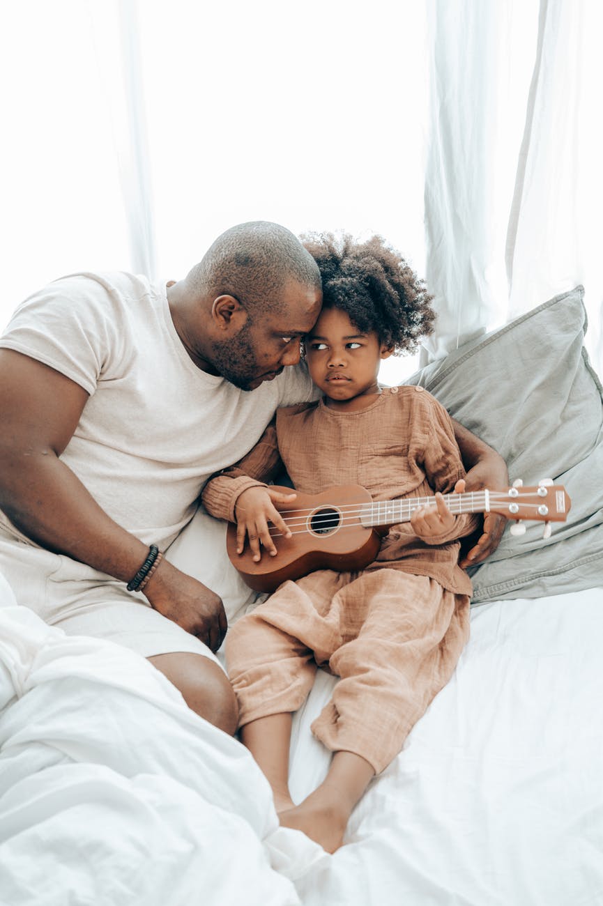 ethnic kid with guitar and father on bed at home